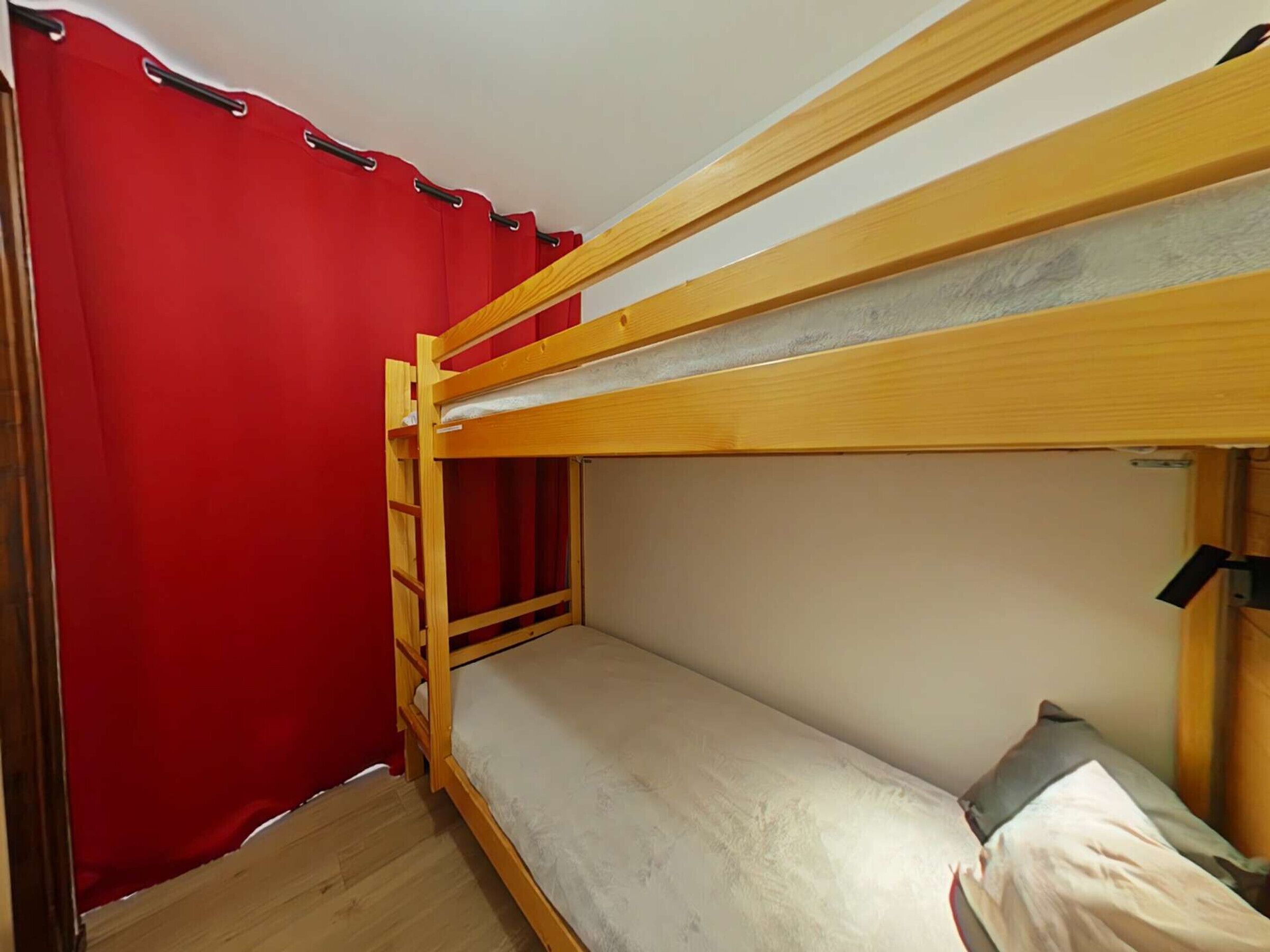 A bunk bed room with a red curtain, wooden ladder, and a single bed with a pillow.