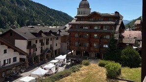A traditional wooden building with a bell tower, surrounded by other buildings and a mountainous backdrop.