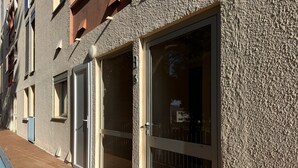 Fachada de edificio con amplios ventanales y puertas de vidrio, terraza de madera y pared con textura.