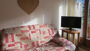 A living room with a sofa, a television on a wooden stand, and a large window with curtains.