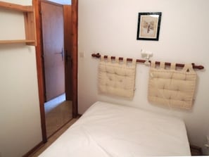 Un dormitorio con puerta de madera, una cama con ropa de cama blanca y dos cabeceros color beige.