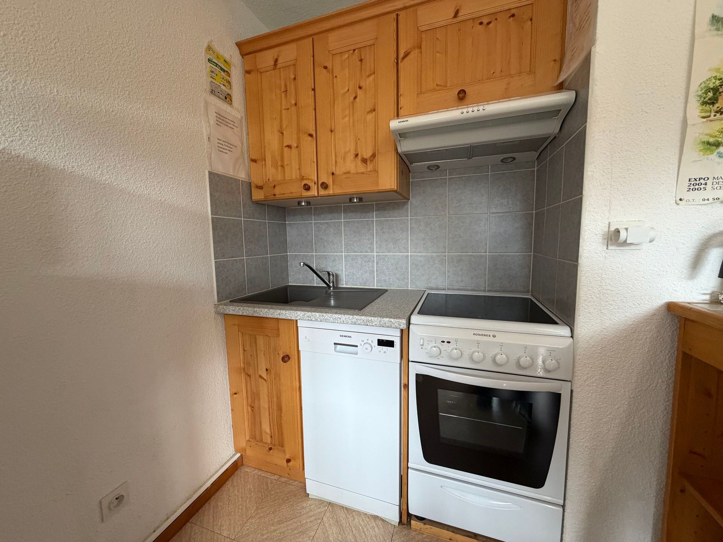 Une cuisine compacte avec des meubles en bois, un lave-vaisselle Siemens, une cuisinière Rosieres et un dosseret carrelé.
