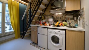 Cozinha compacta com máquina de lavar, cafeteira e diversos produtos frescos na bancada.