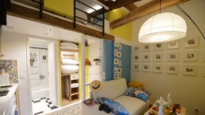 Uma sala de estar aconchegante com um sofá, uma mesa de jantar com comida, uma escada e uma parede com quadros.