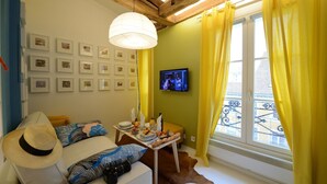 Uma sala de estar acolhedora com um sofá, uma mesa de jantar com uma garrafa e copos, uma televisão e quadros nas paredes.