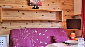 A wooden wall with shelves, a purple sofa with white leaf patterns, a small table with a glass and plate, and a lamp. - Quiet studio cabin, ski-in/out, sleeps 4 - Risoul 1850 (Risoul)