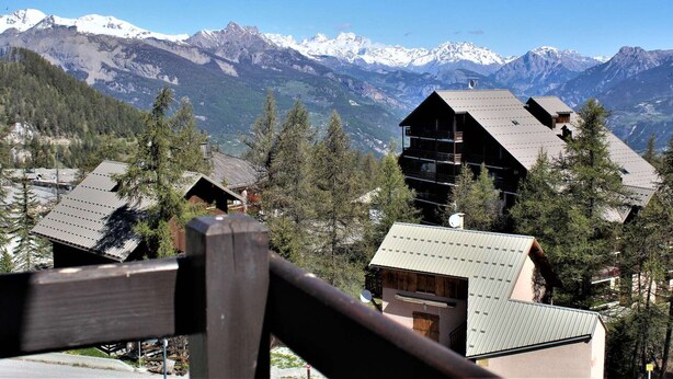 A mountain lodge with a wooden exterior, multiple levels, and a view of snow-capped peaks in the background. - Quiet studio cabin, ski-in/out, sleeps 4 - Risoul 1850 (Risoul)