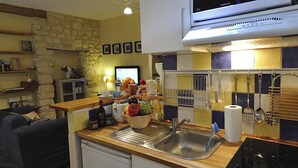 Une cuisine compacte équipée d’un four à micro-ondes encastré, d’un évier et d’une cuisinière. On y trouve des étagères remplies de divers objets et, au fond, un mur en pierre.