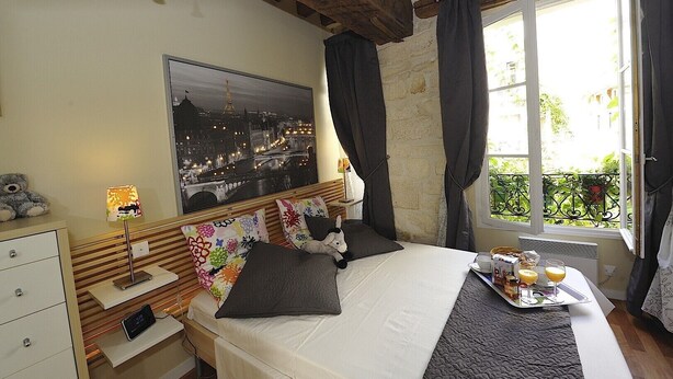 Une chambre à coucher avec un lit, une table de chevet, une lampe, un tableau au mur et une fenêtre avec des rideaux.