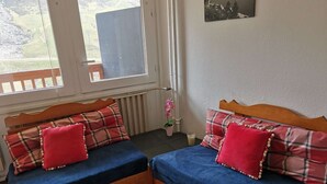 Una habitación con dos camas de madera con ropa de cama azul y roja, una ventana con vistas a un paisaje y una pequeña planta en maceta.