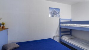 Habitación con una cama individual, colcha azul, mesita de noche con lámpara y un cuadro de una montaña en la pared.