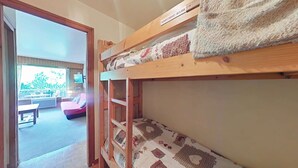 Un lit superposé avec une couvre-lit à motifs, une tête de lit en bois et un panneau indiquant que la chambre est réservée aux enfants de 6 ans et plus.