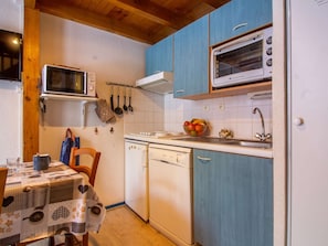 A compact kitchen with a microwave, oven, and sink. There is a table with a patterned tablecloth and a chair.