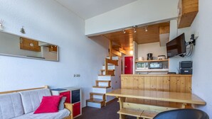 A compact living space with a sofa, a wooden table, a chair, a kitchen area with a TV, and a staircase. - 3-room duplex for 6, valley view, near slopes, pets allowed in Arc 1800 (Les Arcs 1800)