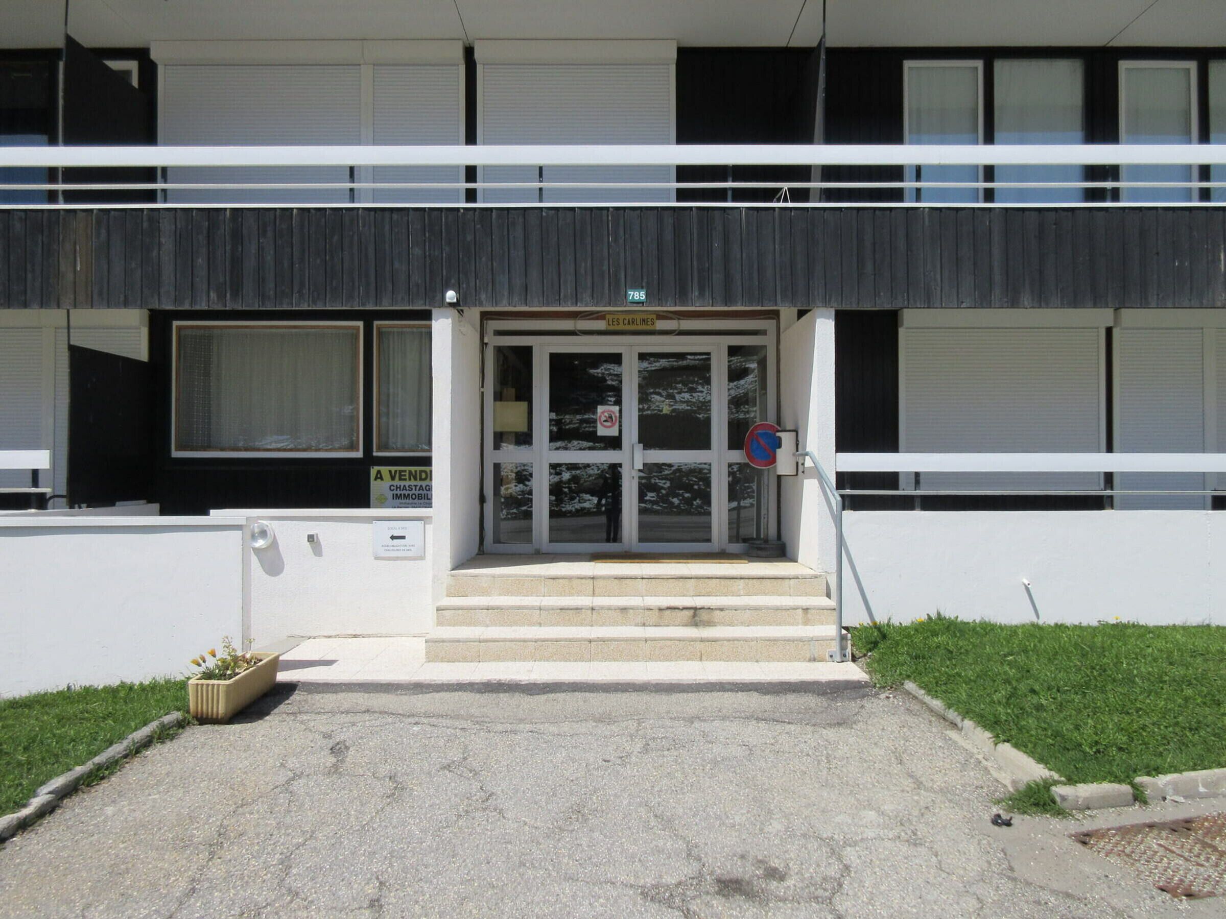 A modern building with a double entrance, a no parking sign, and a sign indicating a sale of real estate.