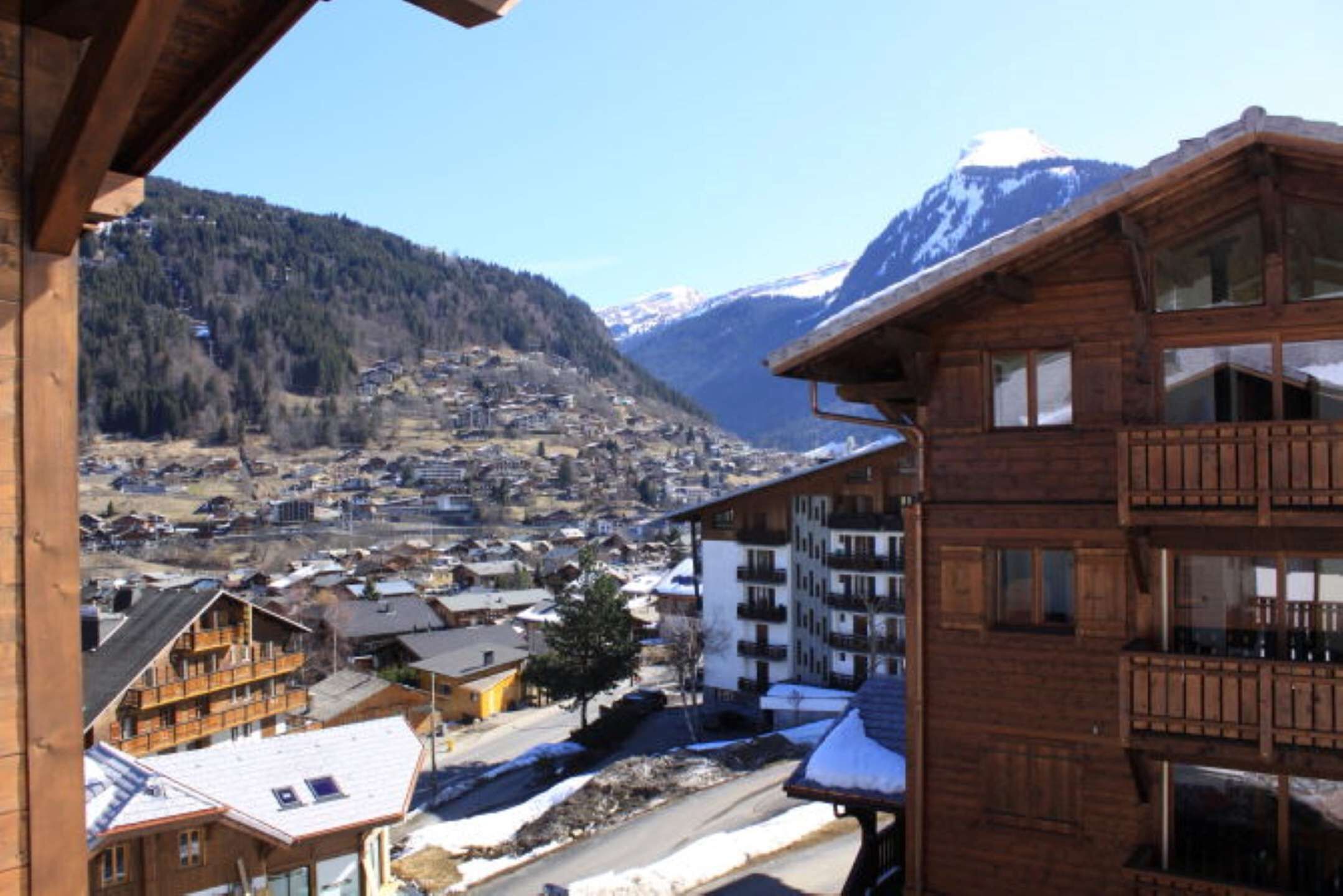 A wooden building with balconies, a town in the valley below, and snow-capped mountains in the background.