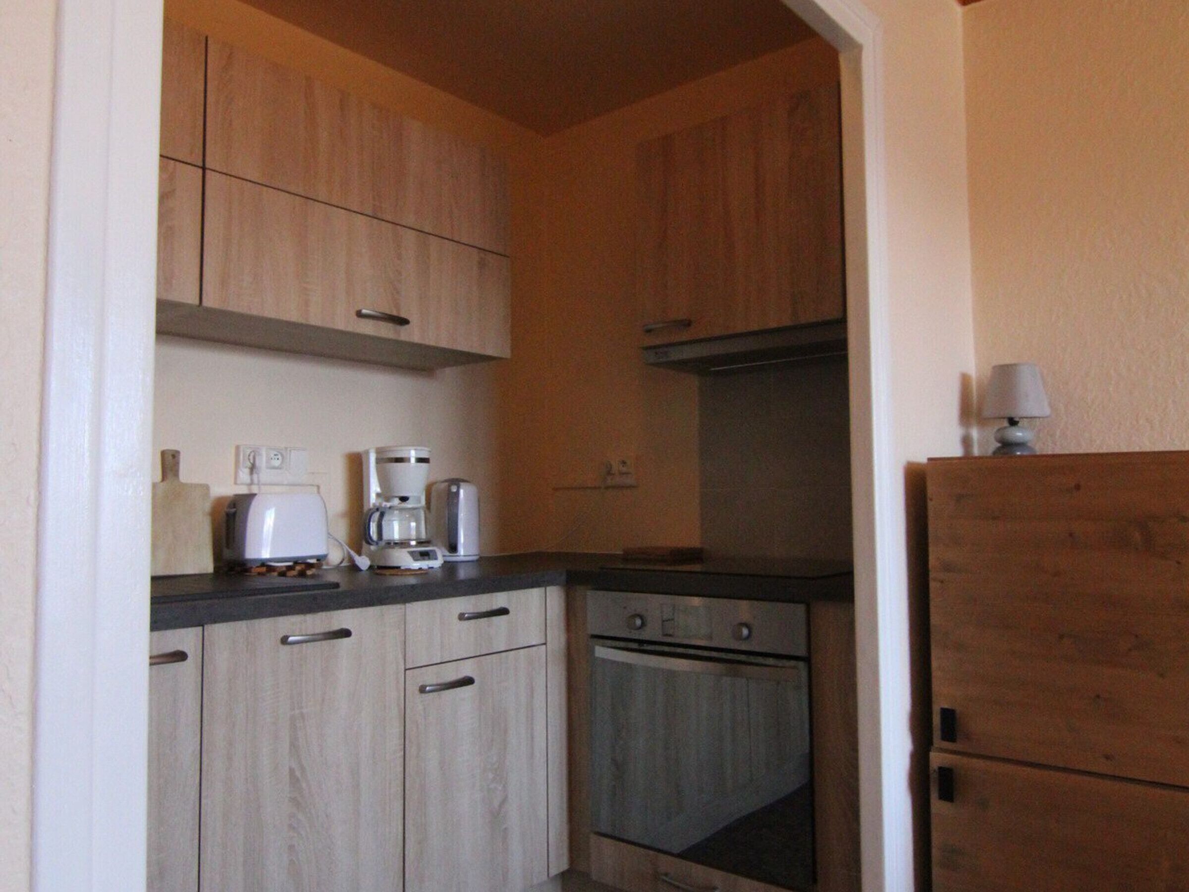 A compact kitchen with wooden cabinets, a built-in oven, a coffee maker, and a refrigerator.