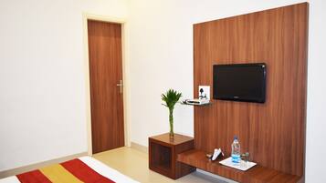 Habitación de hotel con una pared de madera decorativa, un televisor montado, una pequeña mesita de madera con una planta, una botella de agua y un salero.