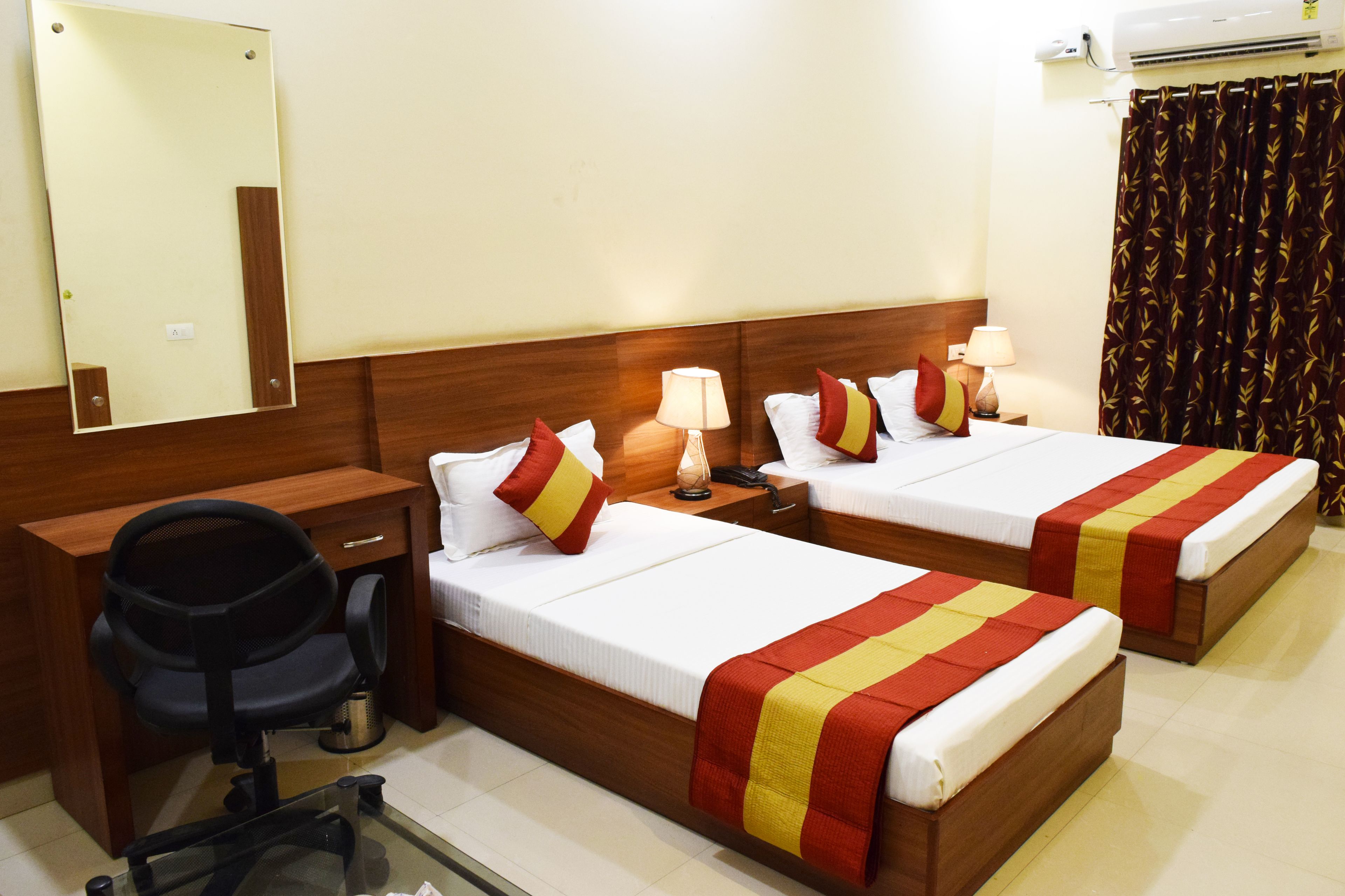 A hotel room with two beds, a desk, a chair, and a mirror.