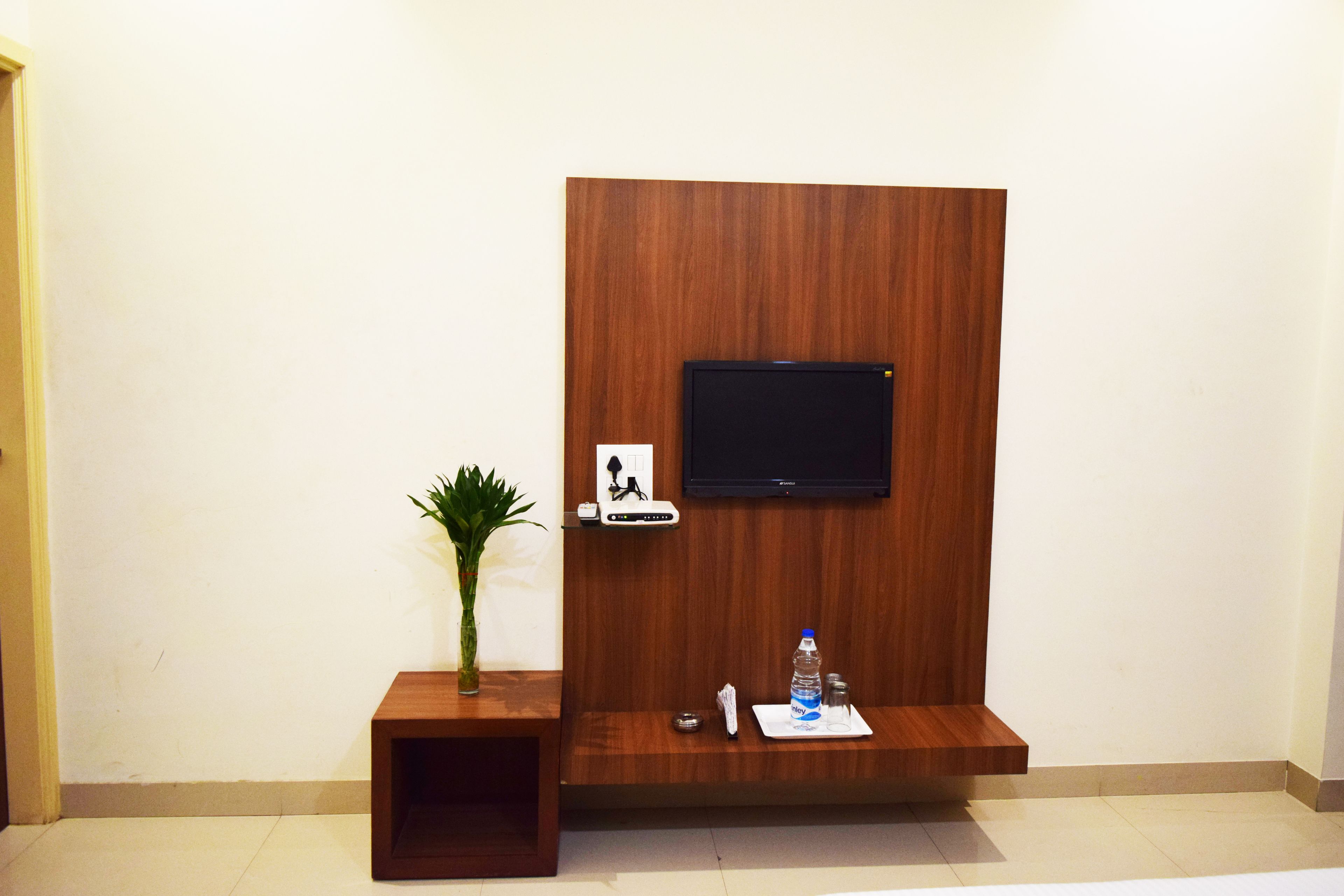 A wooden reception desk with a flat-screen TV, a small plant, a water bottle, and a remote control.