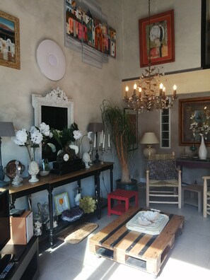 A cozy living room with a wooden coffee table, a red stool, a chandelier, and a variety of decorative items including flowers and a clock.