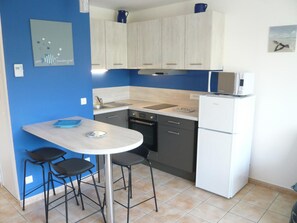 A compact kitchen with a white refrigerator, a microwave, a sink, and a dining area with a table and two chairs.