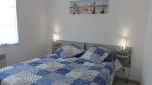 A bedroom with a bed, two bedside lamps, a painting on the wall, and a window. - Private Garden in Barfleur - Ground Floor Apartment (Barfleur)