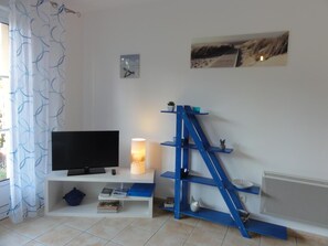 A living room with a TV, a lamp, a blue shelf unit, and a beach-themed picture on the wall.