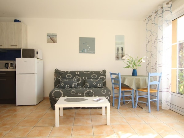 A compact living space with a kitchenette, a sofa, a dining table with chairs, and a small window with curtains.