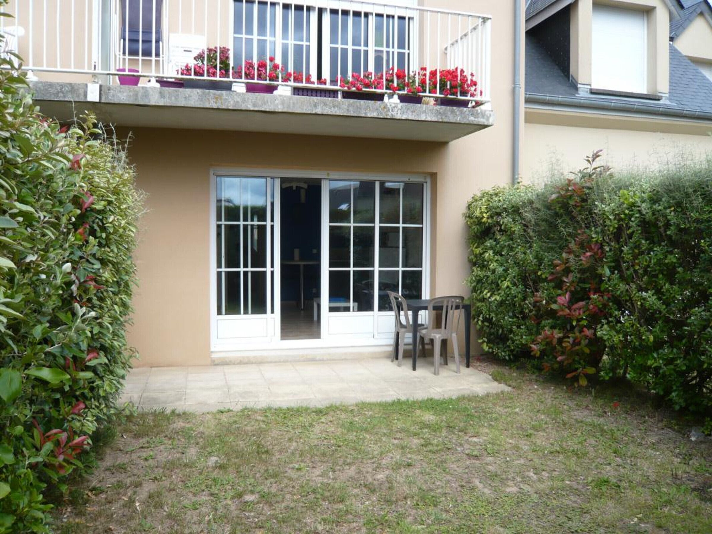 A residential building with a balcony, a sliding glass door, and a small patio area with a table and chairs.