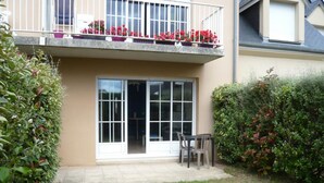 A residential building with a balcony, a sliding glass door, and a small patio area with a table and chairs. - Private Garden in Barfleur - Ground Floor Apartment (Barfleur)