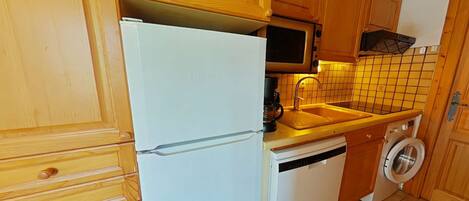 Una cocina compacta con armarios de madera, un refrigerador blanco, un microondas, un lavamanos y una lavadora.