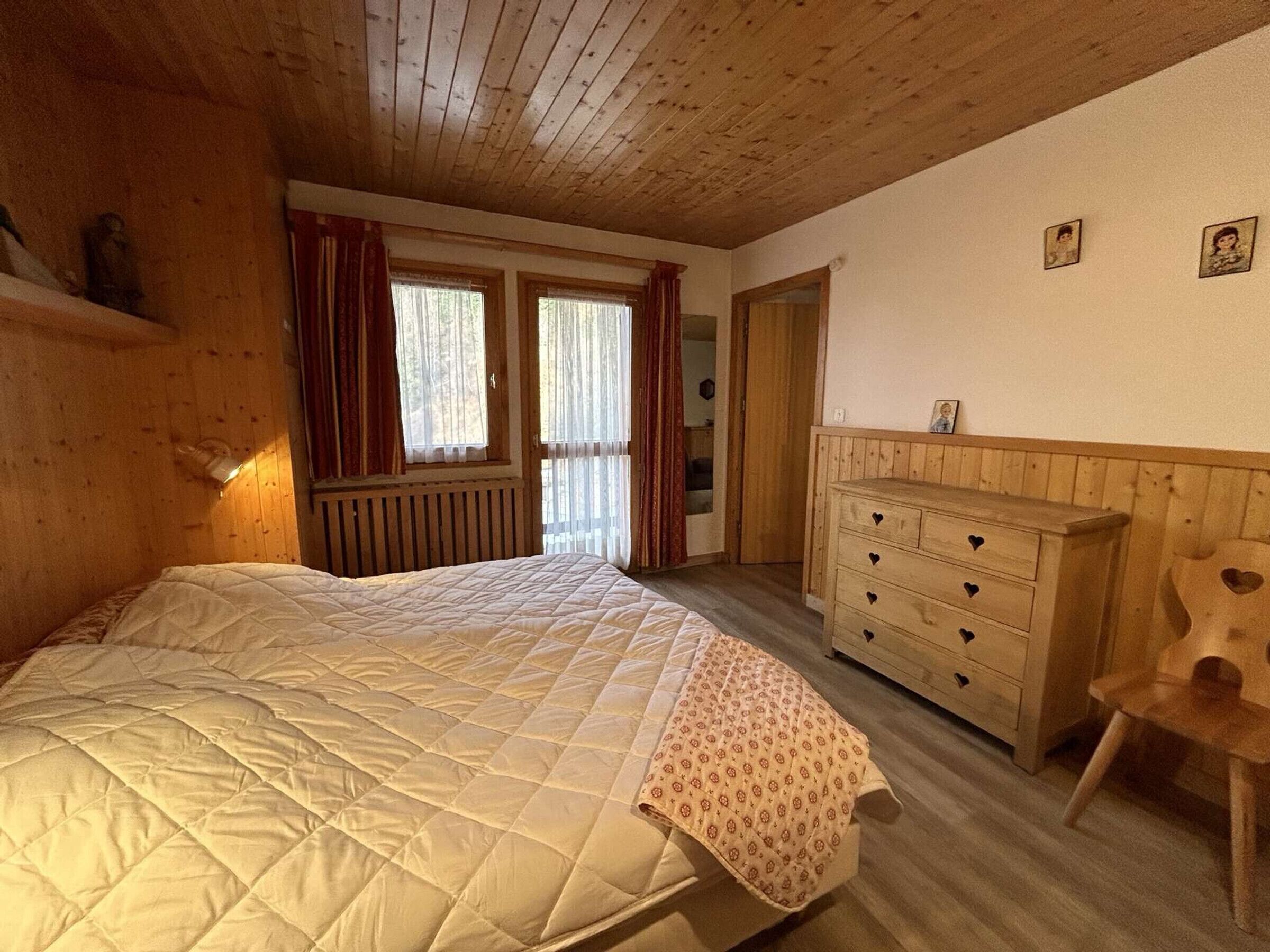 A bedroom with a large bed, wooden dresser, and a window with curtains.