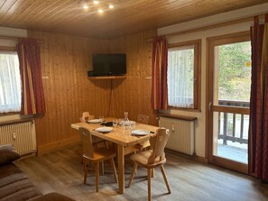 A wooden-paneled room with a dining table set for four, a television mounted on the wall, and large windows with curtains. - Cozy 2-Room Apartment - 100m from Ski Slopes, Near Shops - Pets Welcome (Méribel)