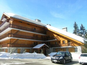 A multi-story wooden lodge with balconies, a stone foundation, and a snow-covered roof.