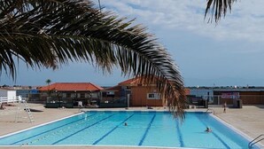 A swimming pool with clear blue water, surrounded by a tiled deck and palm trees. - Cozy Studio Cabine for 4 with Terrace, Pool, and Sports Facilities in Le Barcarès (Port Barcarès)