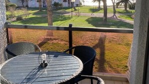 A balcony with a round table and two chairs, overlooking a grassy area with trees and a building in the background. - Cozy Studio Cabine for 4 with Terrace, Pool, and Sports Facilities in Le Barcarès (Port Barcarès)