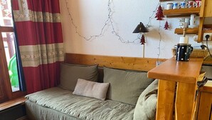 A cozy room with a wooden bench, a wooden table, a sofa with cushions, and a wall decorated with string lights and a small Christmas tree.