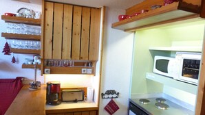 A compact kitchen with wooden cabinets, a microwave, a stove, and various kitchen utensils.