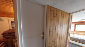 Ett rum med en dörr av trä, en säng med en grå madrass och ett fönster med utsikt över omgivningen.