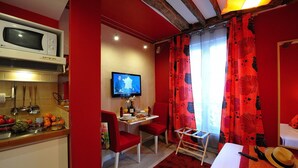 Une chambre d’hôtel compacte comprenant un coin cuisine, un espace repas, une télévision et un lit agrémenté d’un tapis rouge.