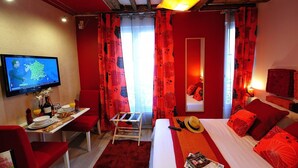 Une chambre d’hôtel aux couleurs rouge et blanc, avec un lit, un bureau et une chaise, une télévision et une fenêtre avec des rideaux.