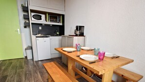 A compact kitchen with white cabinets, a microwave, and a coffee maker. A wooden table with benches is set for dining.
