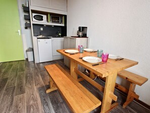 Cocina compacta con armarios blancos, microondas y cafetera. Una mesa de madera con bancos está dispuesta para comer.