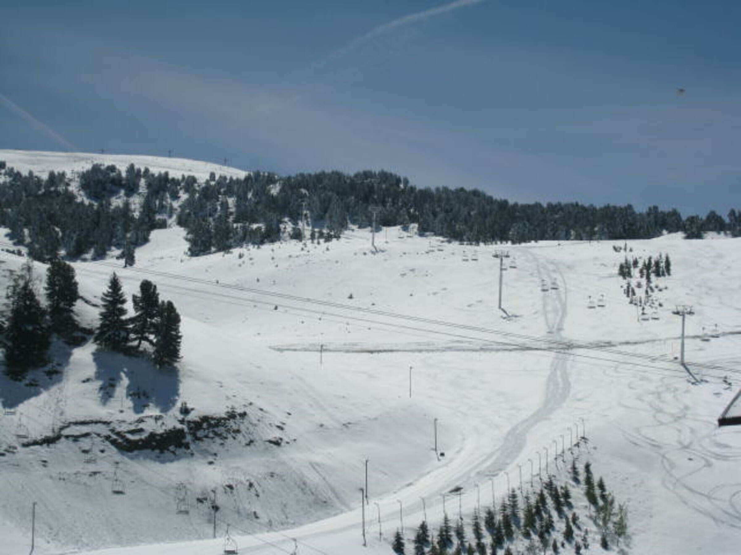 A snow-covered ski slope with ski lifts and trees.