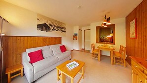 A cozy living room with a grey sofa, red cushions, a wooden coffee table, and a dining area with a wooden table and chairs. - Cozy studio - 4 people, parking, pets allowed (Le Grand-Bornand)