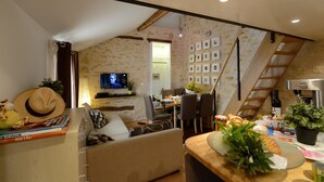 A cozy living room with a television, a dining area with a wooden table and chairs, and a staircase leading to an upper level.