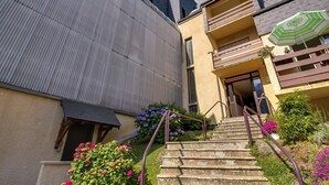 A residential building with a metal roof, a staircase leading to a balcony, and a small garden with flowers. - Cozy 1BR Apartment for 4 with Balcony, Near Ski Lift and Amenities in Cauterets (Cauterets)
