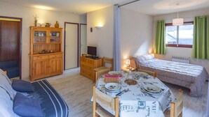 A compact room with a bed, a dining table set for two, a wooden cabinet, and a small table with a lamp. - Cozy 1BR Apartment for 4 with Balcony, Near Ski Lift and Amenities in Cauterets (Cauterets)