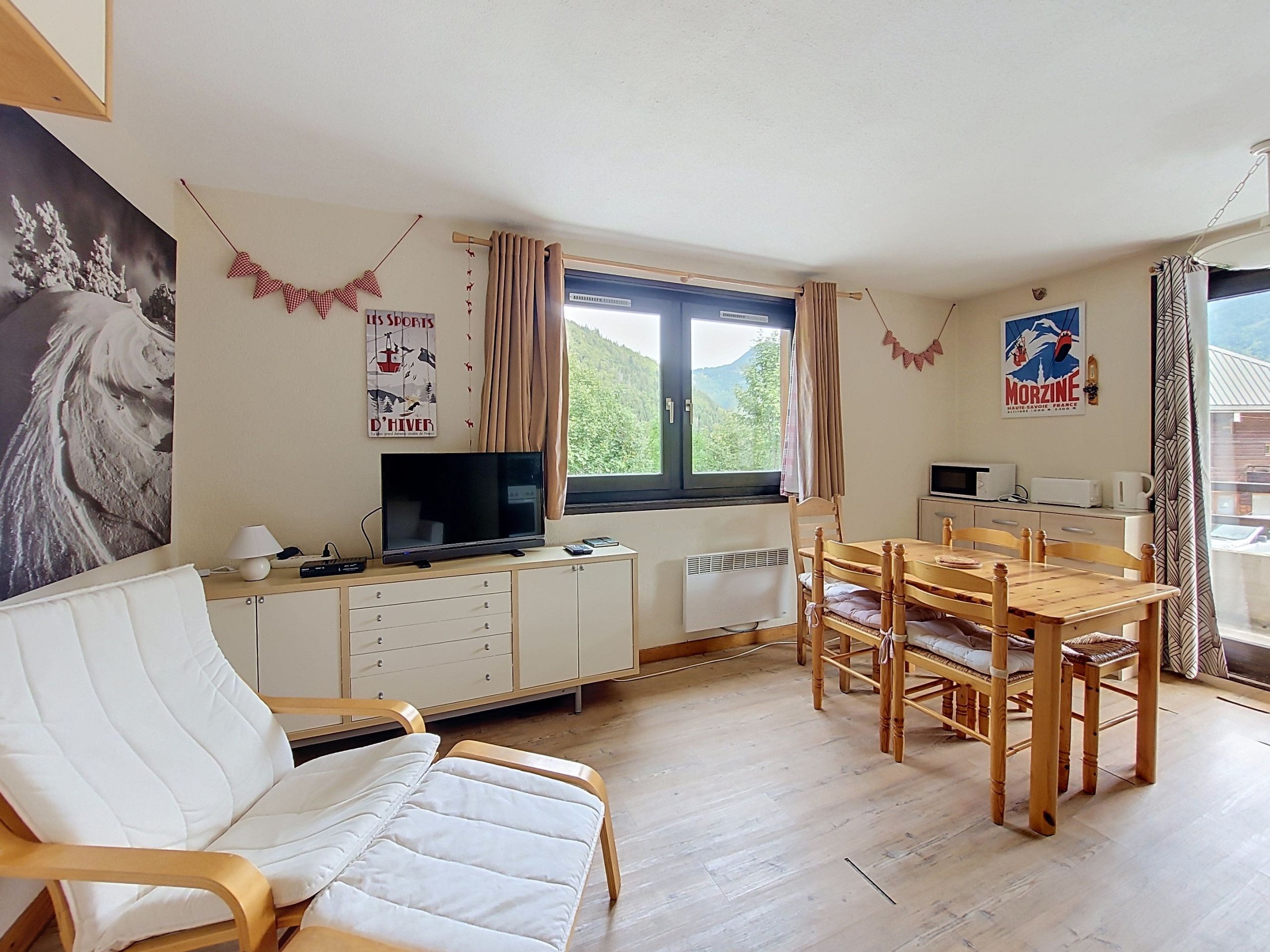 A cozy living room with a sofa, a dining table with chairs, a TV, and a window with curtains.